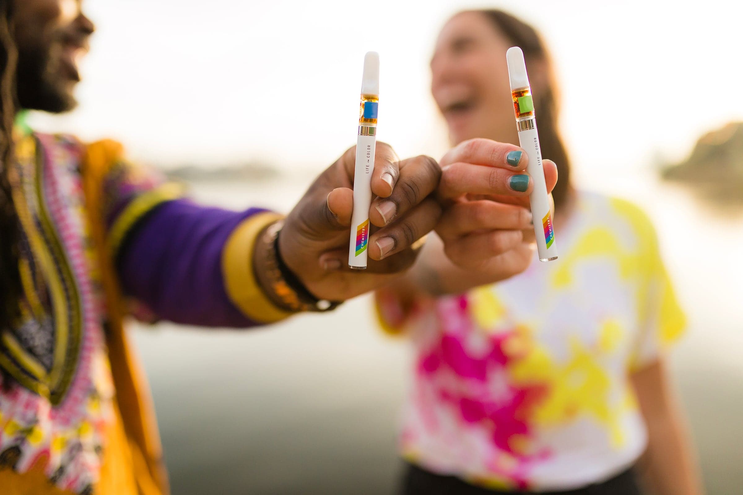 Two smiling people each holding Chemistry vape pens